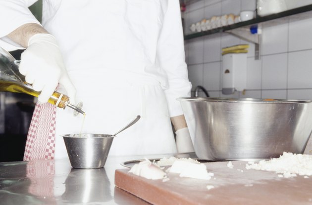 Chef adding olive oil to ingredients in bowl, mid section