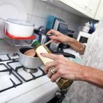 Cropped image of senior woman adding olive oil to saucepan at kitchen counter