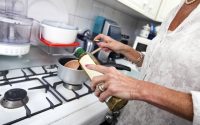 Cropped image of senior woman adding olive oil to saucepan at kitchen counter