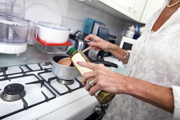 Cropped image of senior woman adding olive oil to saucepan at kitchen counter